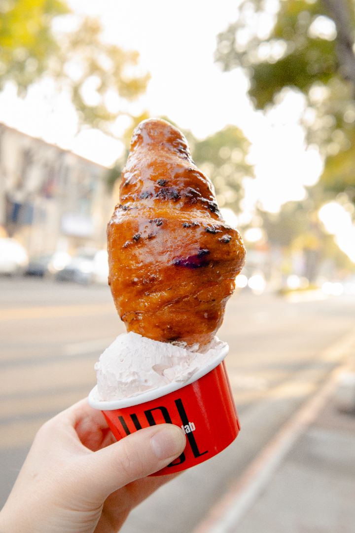 Photo of a hand holding a bruleed croissant with a cup of sea salt creme in broad daylight