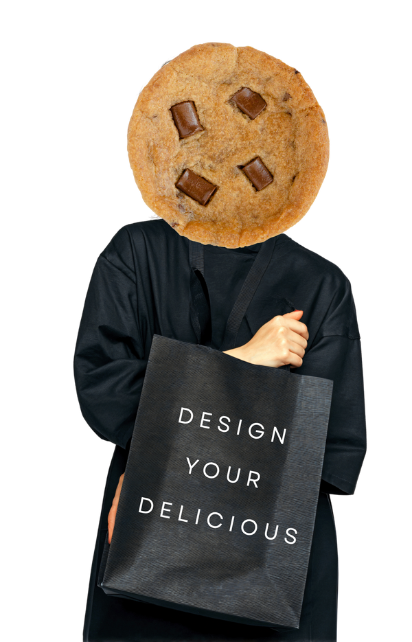 Person wearing a cookie head holding a tote bag with Urban Dessert Lab 'Design Your Delicious' text on a black bag