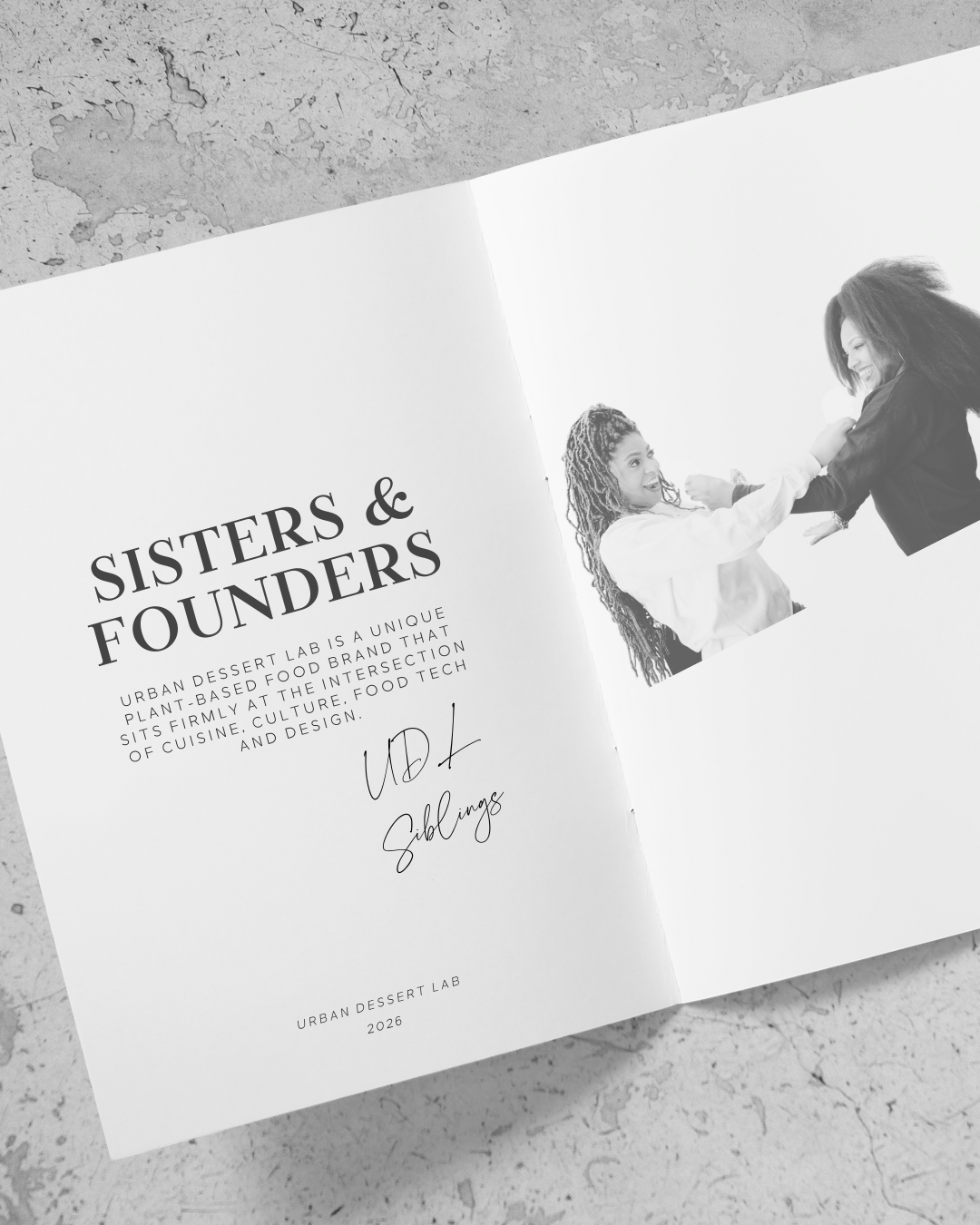 Open book with text and a photo of Urban Dessert Lab founders and sisters on a textured surface