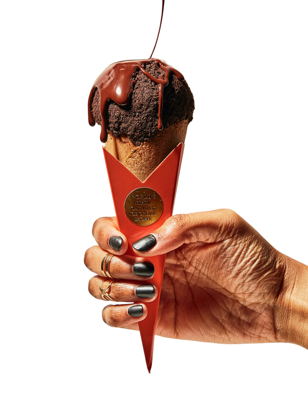 A hand holds a waffle cone filled with ice cream, topped with dripping chocolate - Urban Dessert Lab Ice Cream & Chocolate Sauce